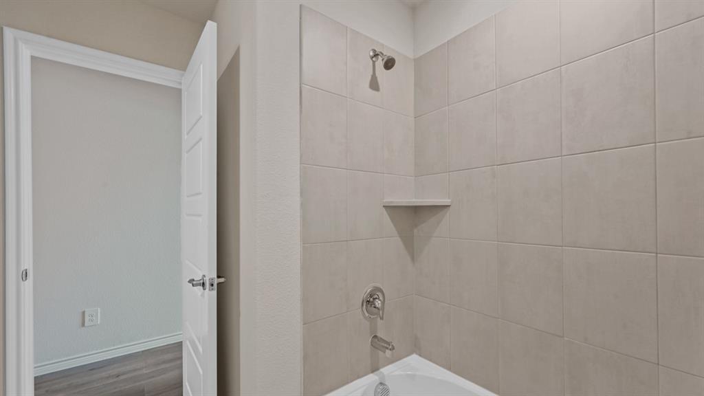 Shower/tub combination with light-toned rectangular tile surround, built-in corner shelf, and chrome fixtures
