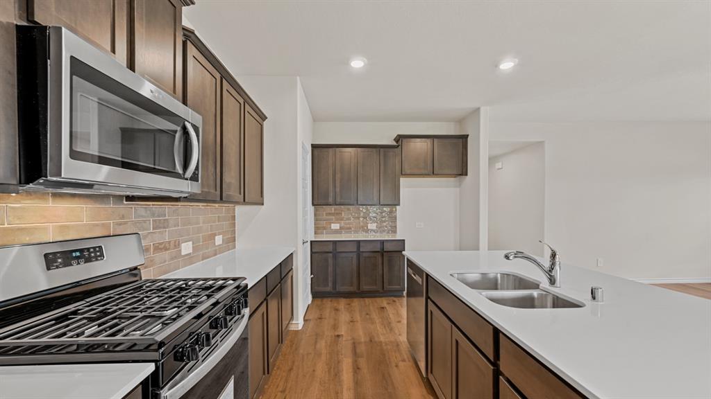 Kitchen featuring wood-finish flooring, stainless steel appliances, dark wood cabinetry, white countertops, and a double basin sink