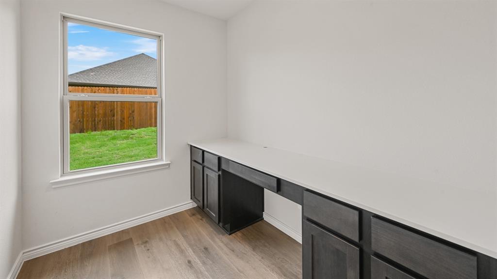 Integrated desk with dark wood-finish cabinetry and light-toned countertop, wood-finish flooring, and a window with white trim