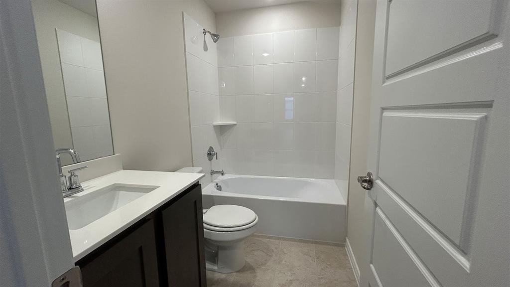 Bathroom featuring a vanity with a white countertop and rectangular undermount sink, dark-finish cabinetry, a white tub-and-shower combination with tiled surround, and tile flooring