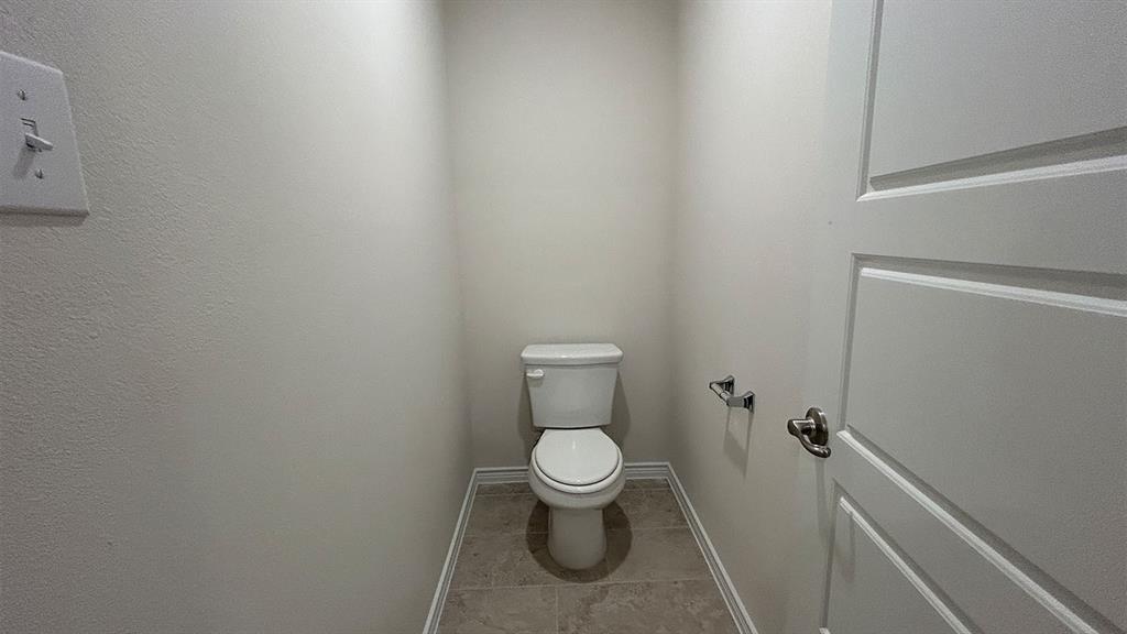Neutral-toned restroom featuring a white toilet, tiled flooring, and a paneled interior door with metallic hardware