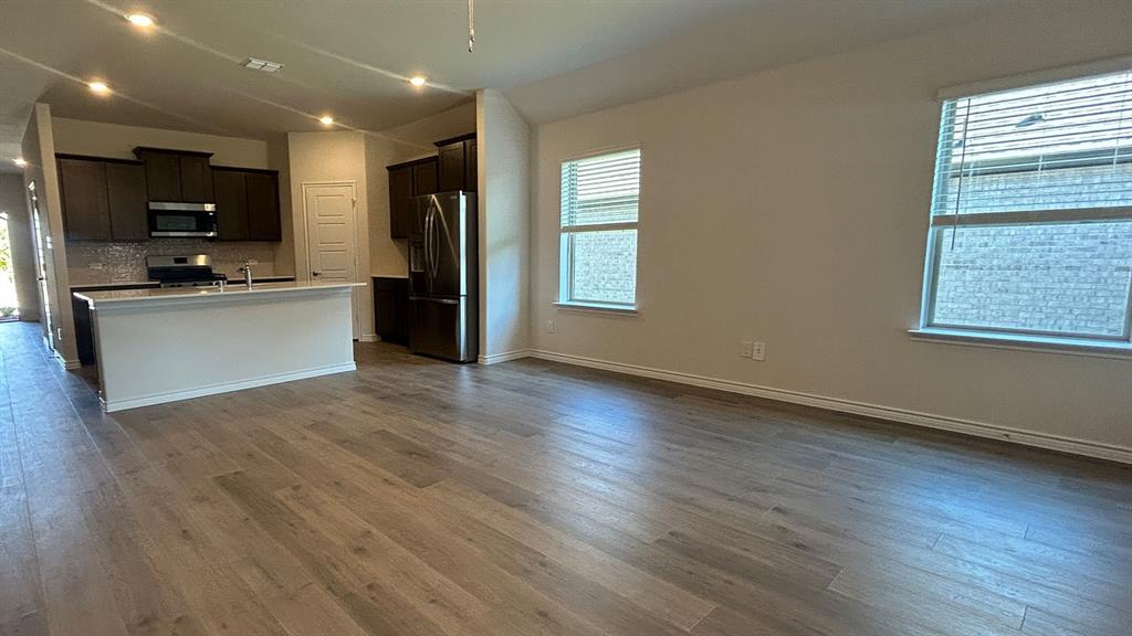 Open-concept interior featuring wood-finish flooring, recessed lighting, and a kitchen with dark cabinetry, stainless steel appliances, and a quartz-topped peninsula