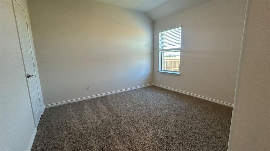 Interior room featuring neutral-toned carpeting, vaulted ceilings, and a single window with fitted blinds