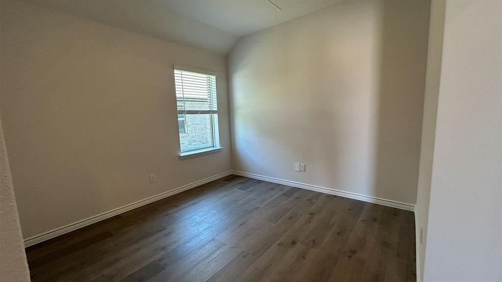 Room featuring vaulted ceilings, wood-finish flooring, and natural light from a single window