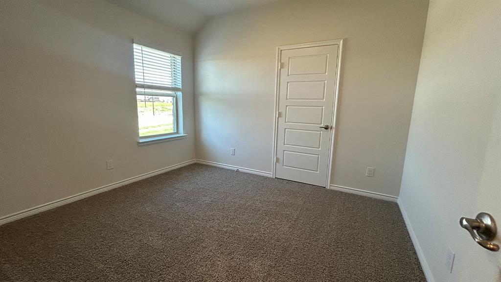 Neutral interior featuring high-vaulted ceilings, neutral carpeting, a single-hung window with horizontal blinds, and a five-panel interior door with satin-finish hardware
