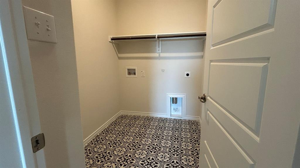 Utility area featuring patterned ceramic tile flooring, a wall-mounted shelving unit, and recessed plumbing hookups