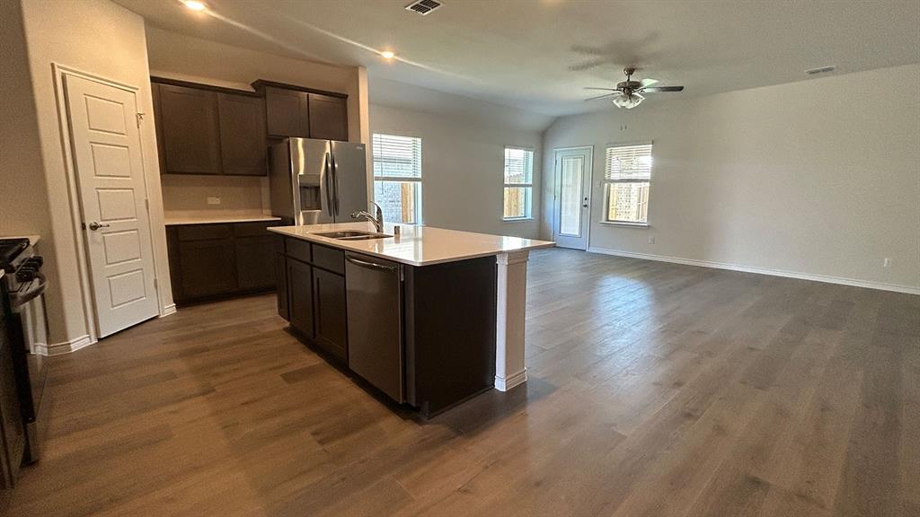 Kitchen featuring dark wood-finish cabinetry, a central island with a stone-surface countertop, stainless steel appliances, and wood-finish flooring
