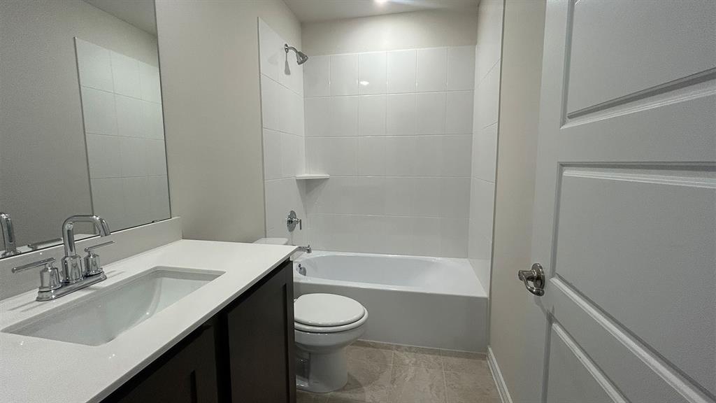 Dark cabinetry vanity with a solid-surface countertop and integrated sink, complemented by a white-tiled shower-tub combination and a large wall-mounted mirror