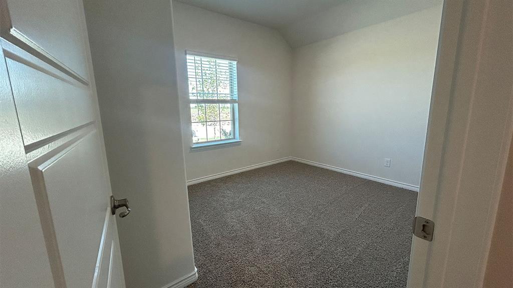 Neutral-toned room featuring neutral carpeting, a single-panel window with muntins, a vaulted ceiling, and a multi-panel door with metallic hardware