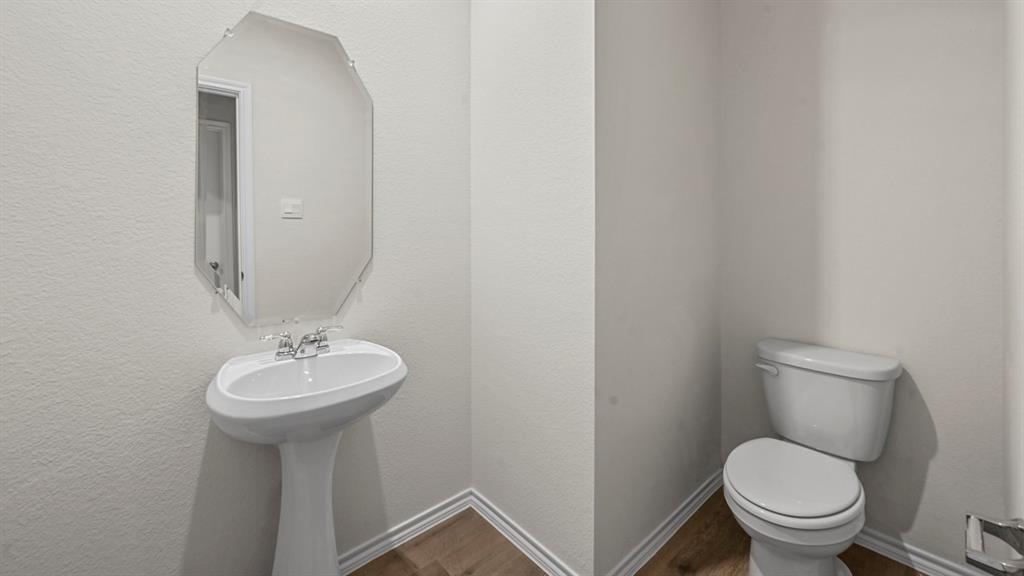Pedestal sink with chrome faucet, octagonal mirror, toilet, and wood-finish flooring