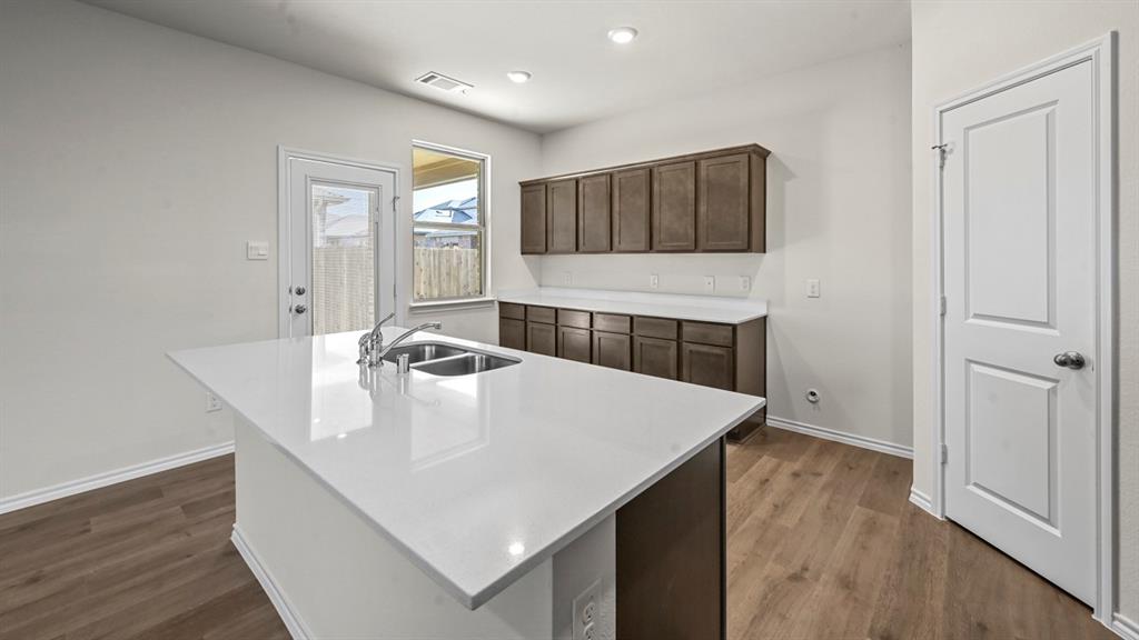 Kitchen island with a double basin sink and chrome faucet, wood-finish flooring, white countertops, and dark wood-finish cabinetry
