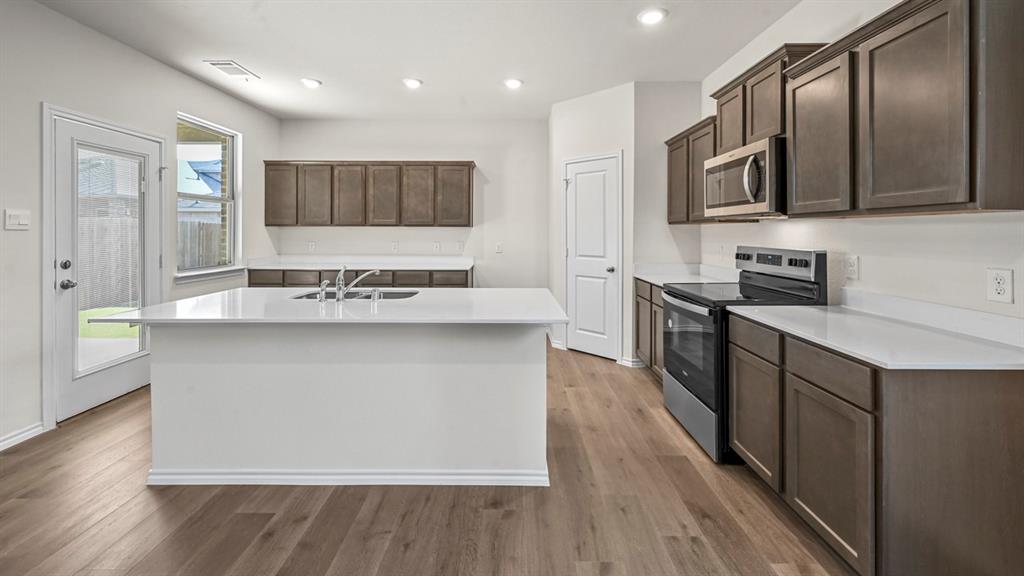 Kitchen featuring a central island with an integrated sink, wood-finish flooring, stainless steel appliances, white countertops, and recessed lighting