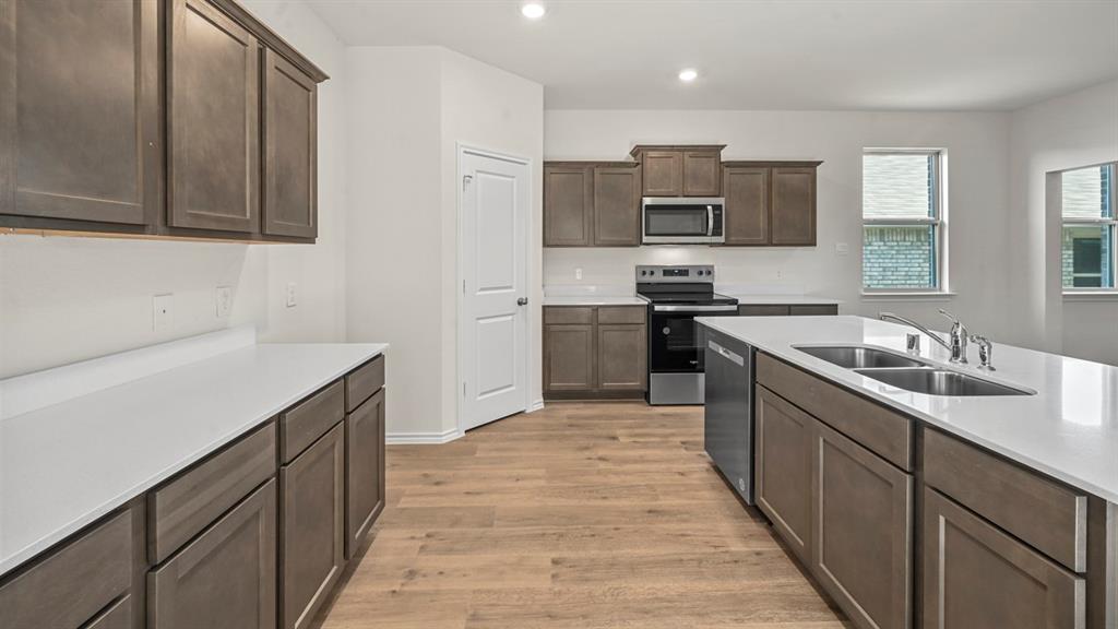 Kitchen featuring an expansive island with a double basin sink, stainless steel appliances, wood-finish flooring, white countertops, and shaker-style cabinetry