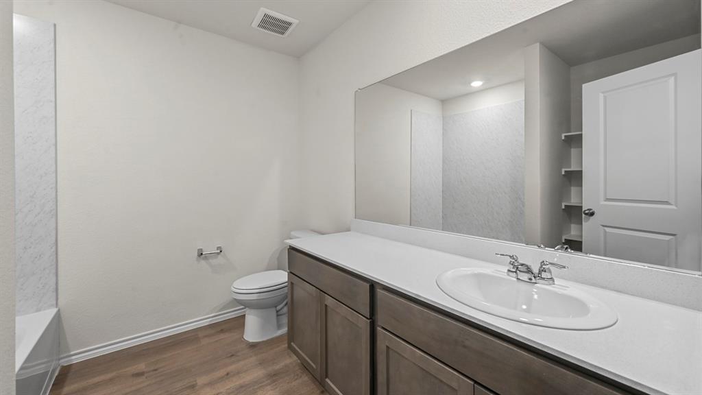 Bathroom featuring a wood-finish flooring, a vanity with a white countertop and integrated sink, a large wall-mounted mirror, and a built-in shower/tub combination with a tiled surround