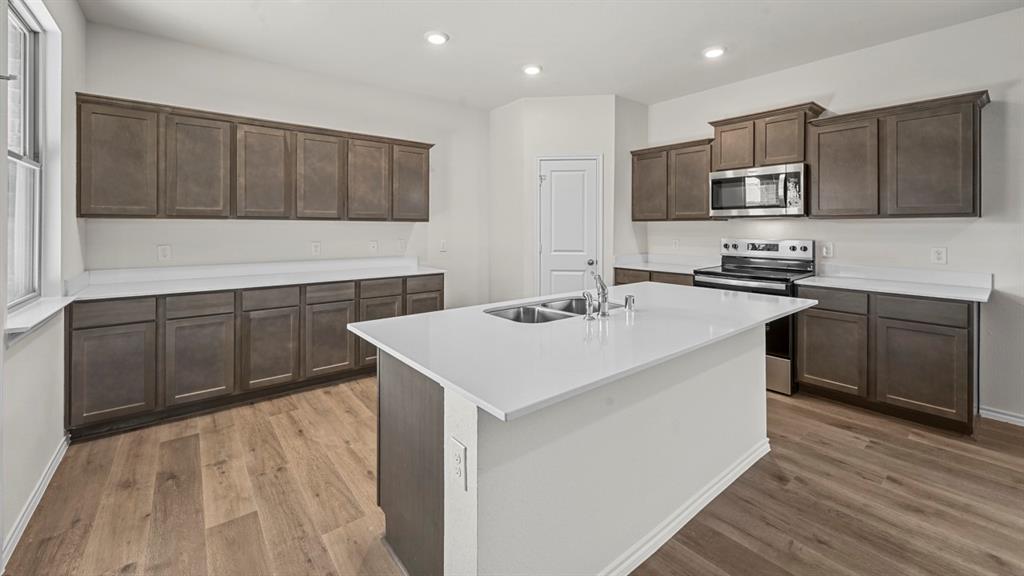 Kitchen featuring an island with dual sinks, extensive dark wood-finish cabinetry, light-toned countertops, stainless steel appliances, and recessed lighting