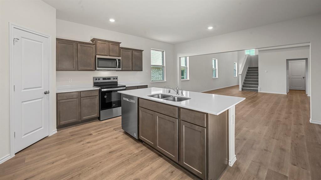Spacious kitchen featuring an island with a double basin sink, stainless steel appliances, dark wood-finish cabinetry, and light-tone wood-finish flooring