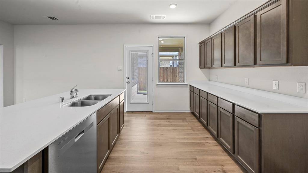 Modern kitchen with extensive dark wood-finish cabinetry, light-toned countertops, a stainless-steel dishwasher, and wood-finish flooring