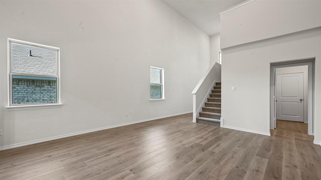 High vaulted ceilings, wood-finish flooring, two large windows, a carpeted staircase, and a paneled interior door