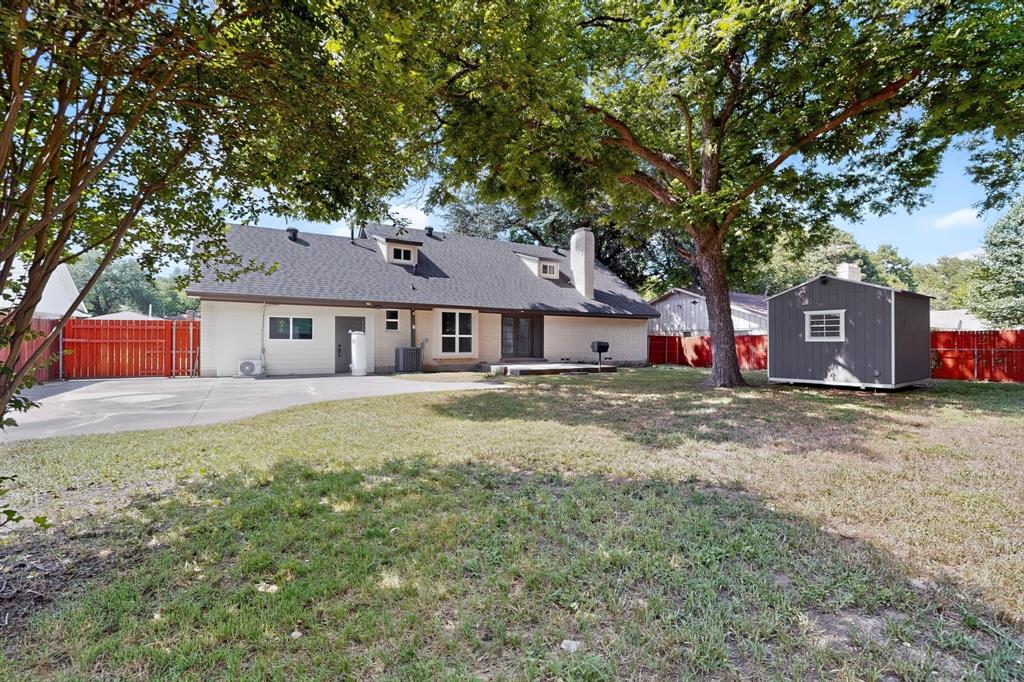 Expansive backyard featuring a concrete patio, mature trees, a detached storage shed, and perimeter privacy fencing