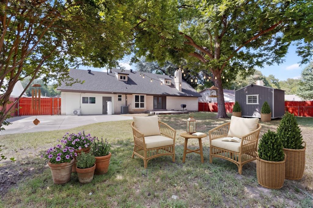 Expansive backyard featuring a concrete patio, mature shade trees, a detached storage structure, and perimeter fencing