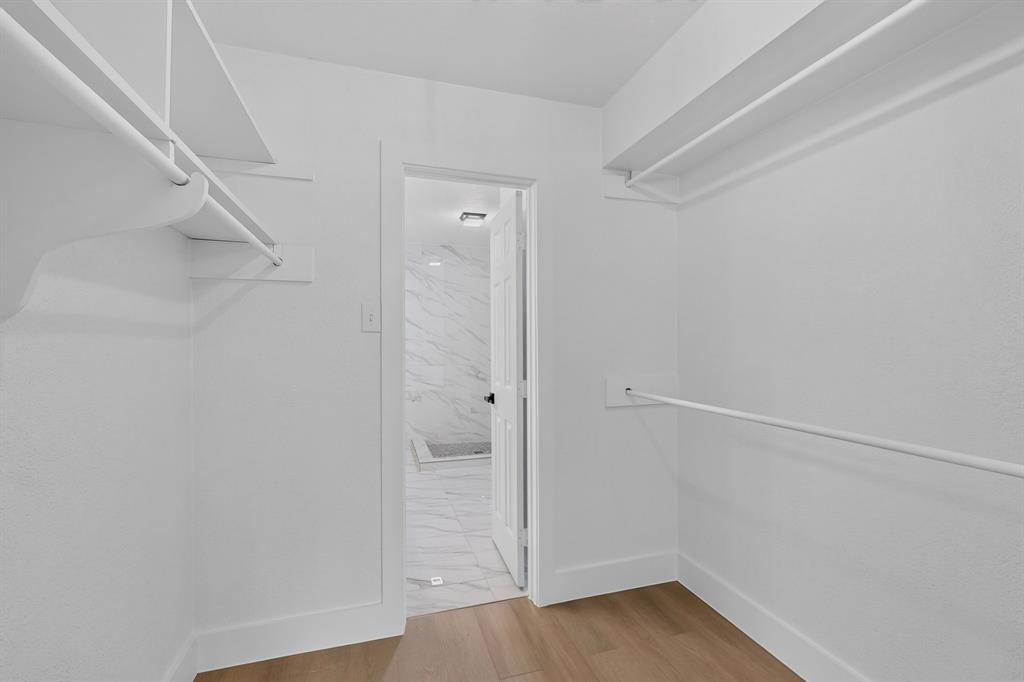 Walk-in closet featuring white built-in shelving, hanging rods, and wood-finish flooring