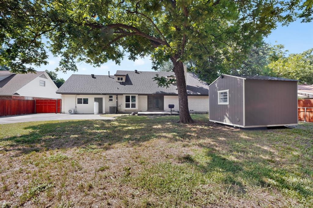 Expansive backyard featuring a mature shade tree, detached storage structure, concrete driveway, and wooden perimeter fencing