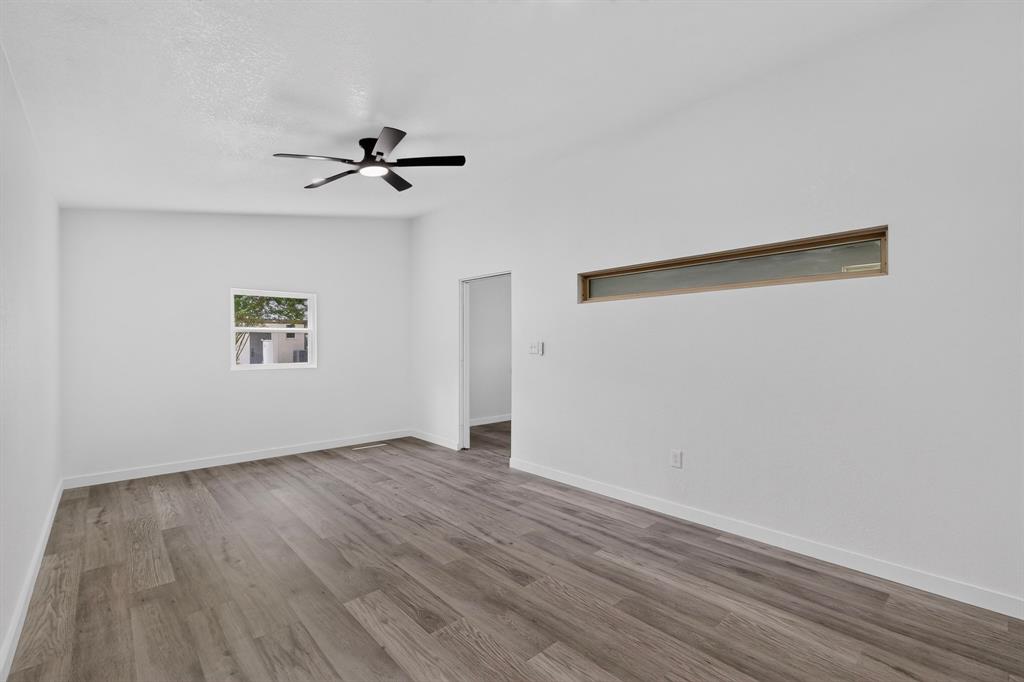 Room featuring wood-finish flooring, white walls, a multi-blade ceiling fan, a horizontal clerestory window, and a standard square window
