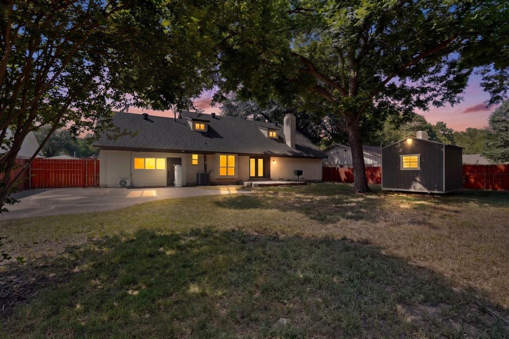 Spacious backyard featuring mature trees, a concrete patio, a detached storage shed, and perimeter wood fencing