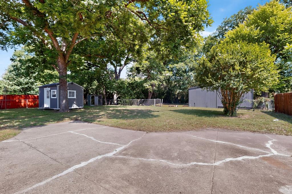 Expansive backyard featuring mature trees, a concrete parking area, a detached storage structure, and perimeter fencing