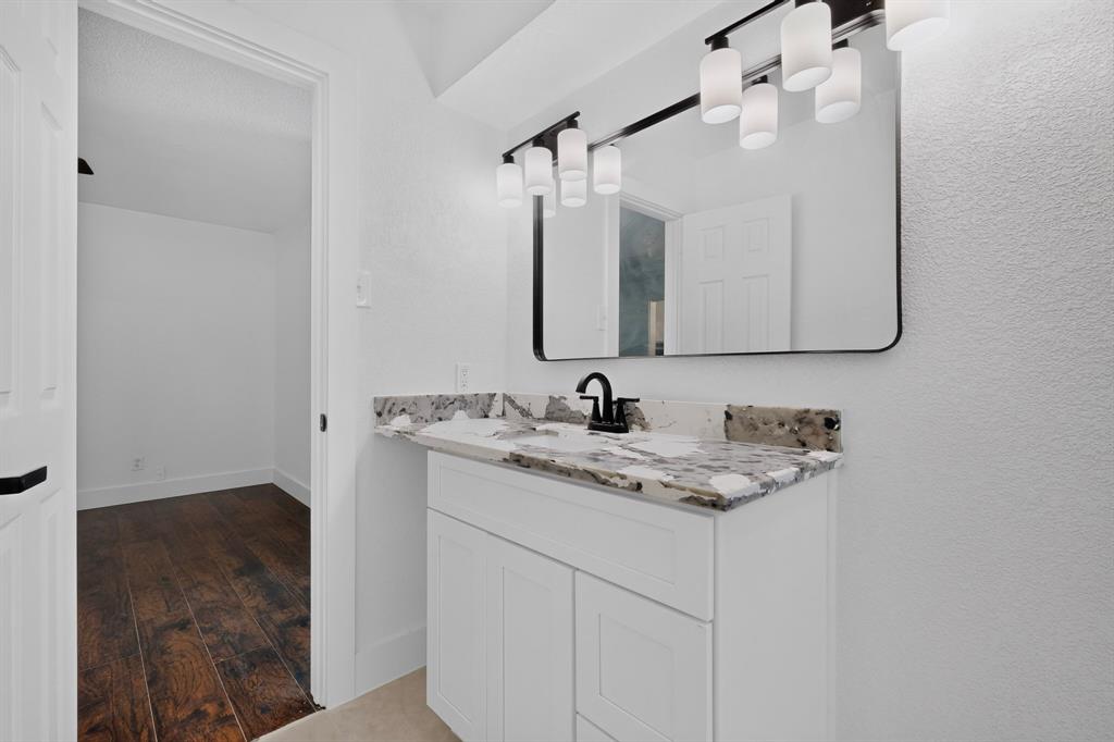 White vanity featuring stone-finish countertop with undermount sink, matte black faucet, wall-mounted rectangular mirror, and five-light vanity fixture