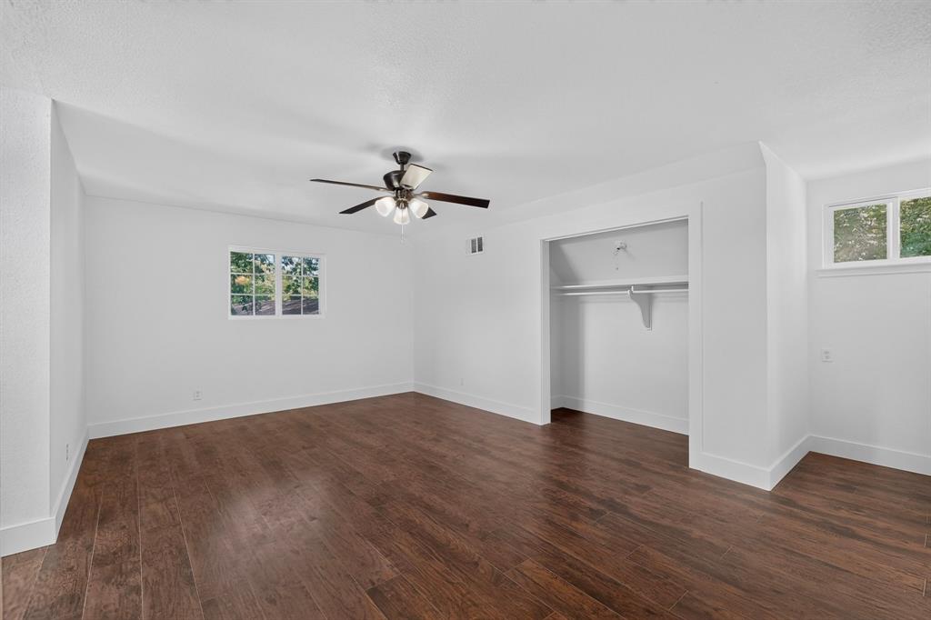 Spacious room featuring wood-finish flooring, recessed closet with built-in shelving, multi-pane windows, and a ceiling fan with integrated lighting