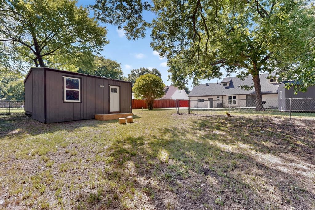 Expansive backyard featuring a detached structure with siding, chain-link perimeter fencing, mature trees, and a multi-section roofline