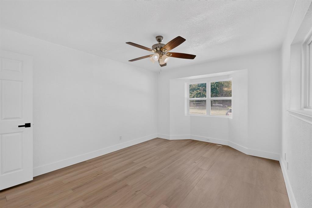 Room featuring wood-finish flooring, a bay window, a ceiling fan with integrated lighting, and a door with matte black hardware