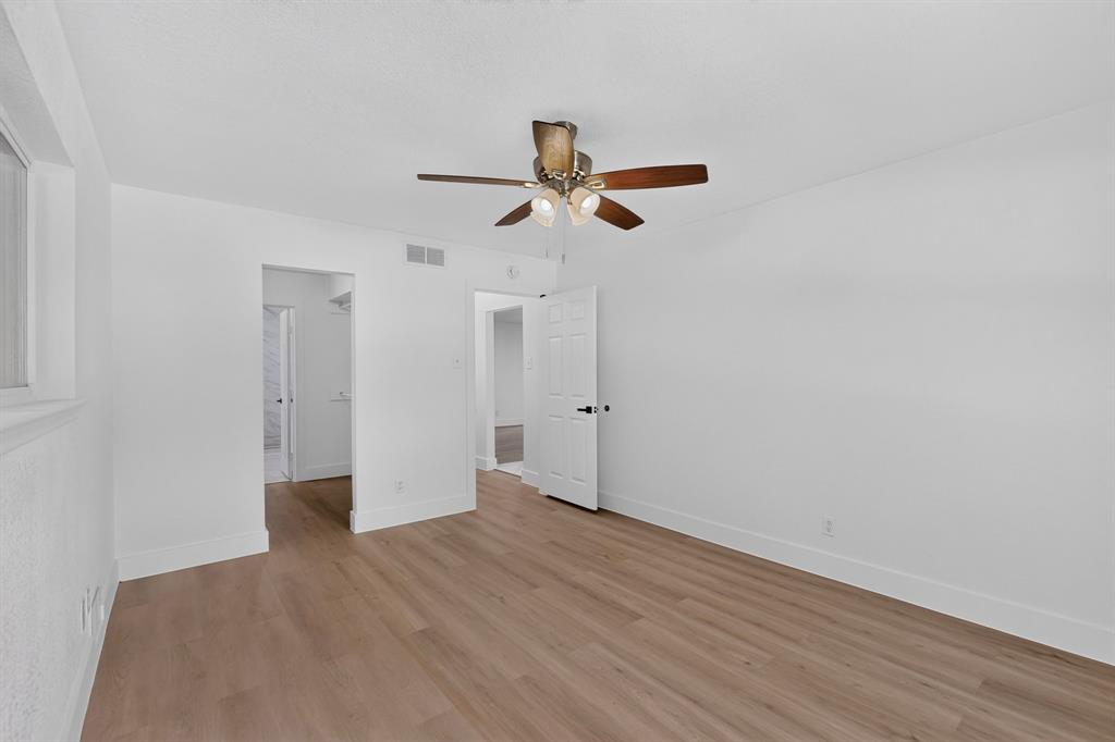 Room featuring wood-finish flooring, white walls, and a ceiling-mounted fan with integrated lighting