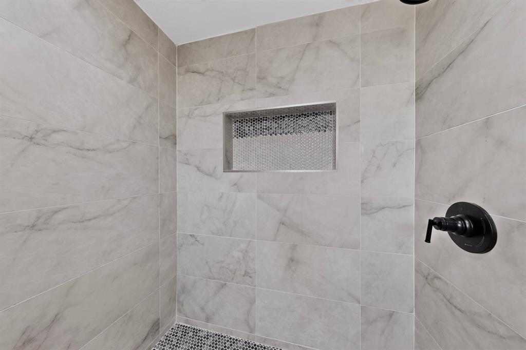 Shower enclosure featuring large-format stone-patterned wall tile, a recessed tile niche with hexagonal accent mosaic, a circular black shower control valve, and a hexagonal tile floor