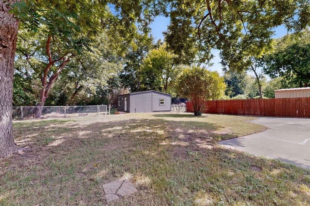 Expansive backyard featuring a concrete driveway, detached storage structure, mature trees, and combination metal and wood-style fencing