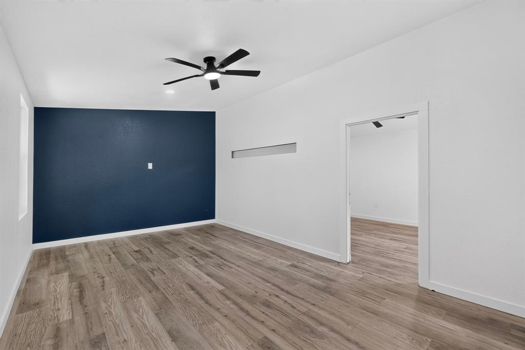 Interior space featuring wood-finish flooring, a dark-toned accent wall, a central ceiling fan with integrated lighting, and a horizontal transom window