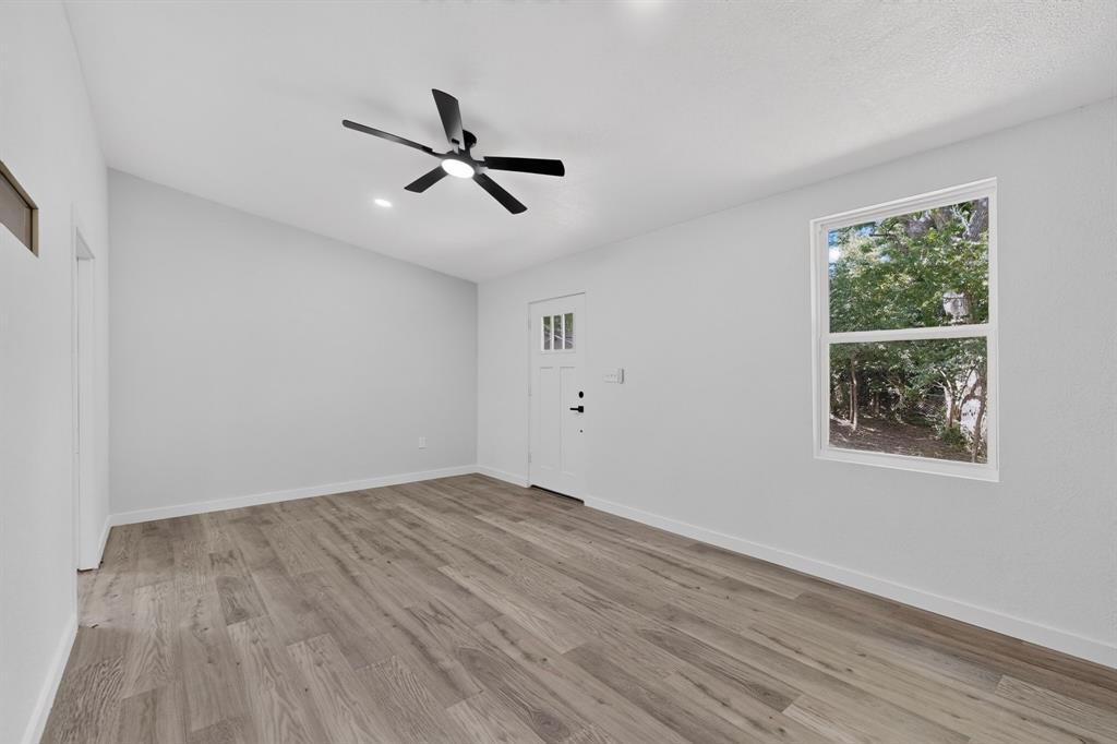 Room featuring wood-finish flooring, a matte black multi-blade ceiling fan with integrated light, a single-hung window, and a door with three-lite glazing