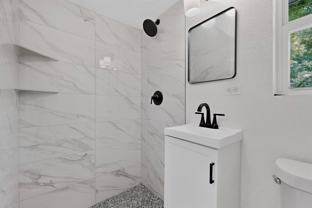 Shower featuring large-format veined tile walls and a built-in shelf, complemented by a pedestal vanity with a matte black faucet and a wall-mounted mirror