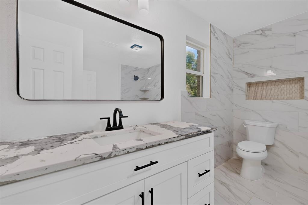 Bathroom featuring a white vanity with stone-finish countertop, undermount sink with matte black widespread faucet, rectangular mirror with black frame, and tiled walk-in shower with recessed niche