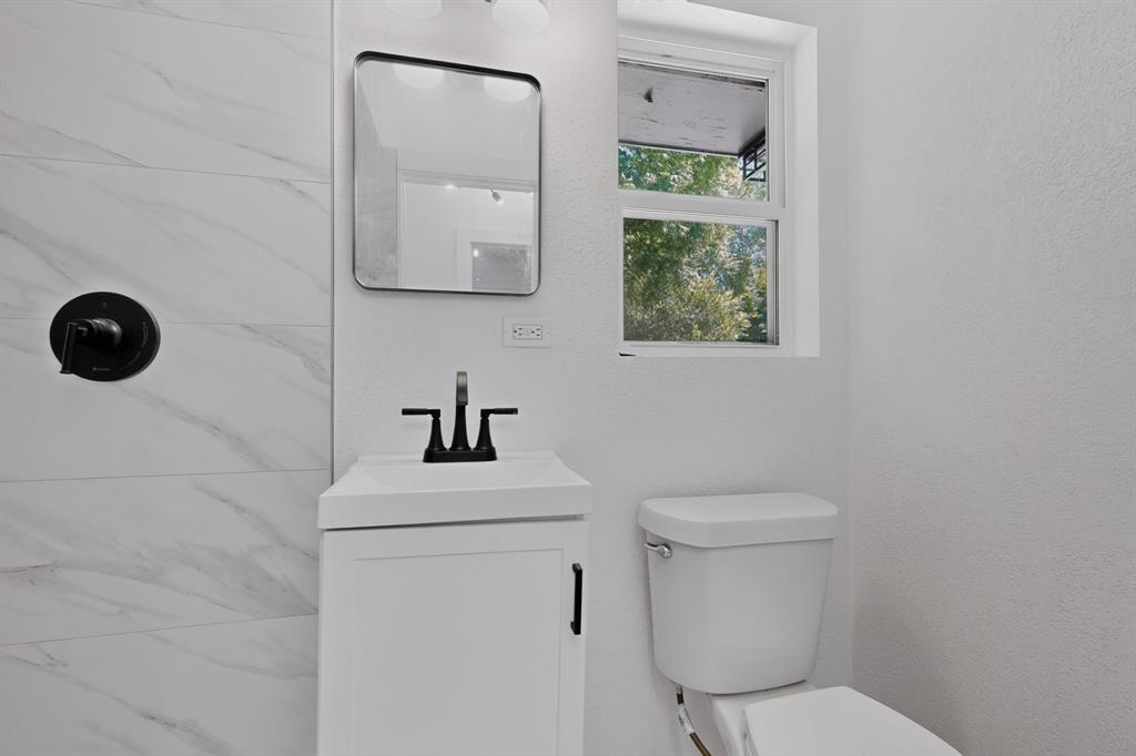 Bathroom featuring a white vanity cabinet, rectangular sink with matte black faucet, wall-mounted mirror, matte black shower handle, and tile surround with marbled finish
