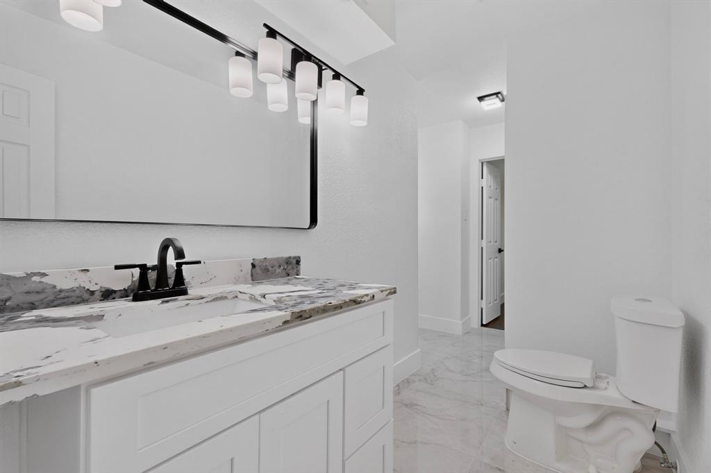White cabinetry with stone-finish countertop, undermount sink, matte black faucet, six-light vanity fixture, and large rectangular mirror
