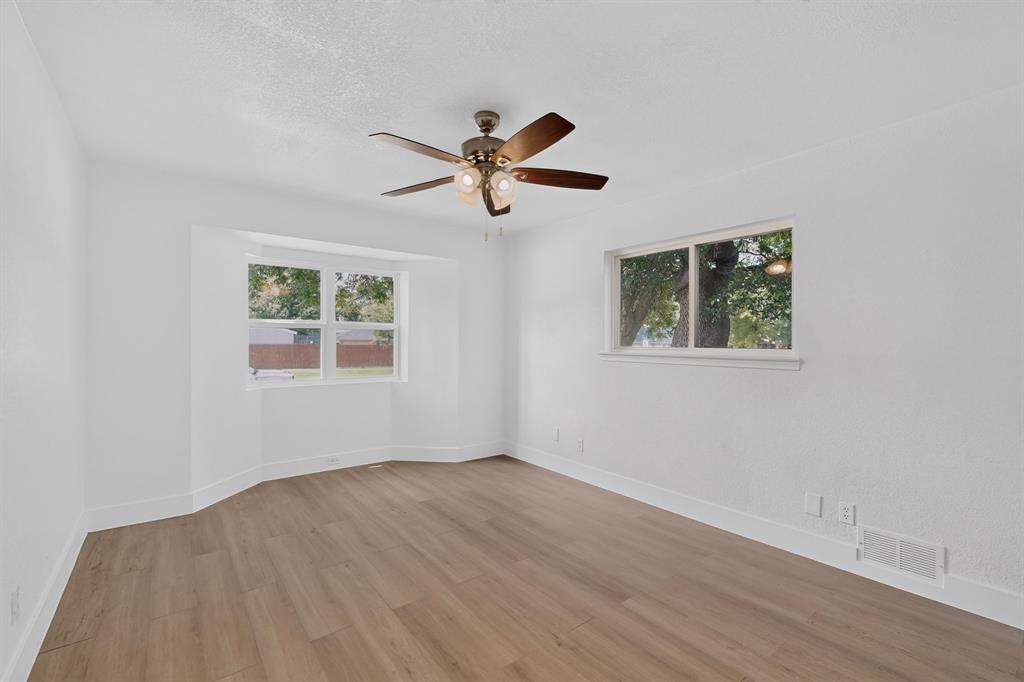 Room featuring wood-finish flooring, a bay window, a dual-pane window, and a multi-blade ceiling fan with integrated lighting