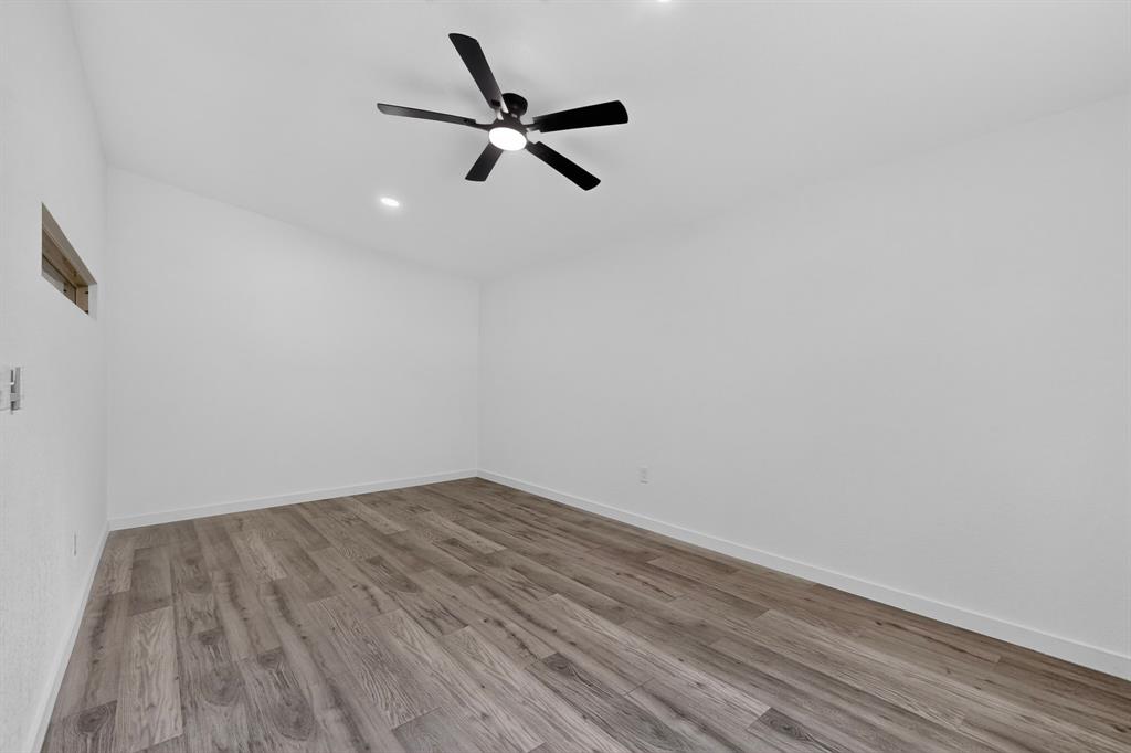 Interior space featuring wood-finish flooring, white walls, high ceiling, recessed lighting, and a matte black ceiling fan with integrated light
