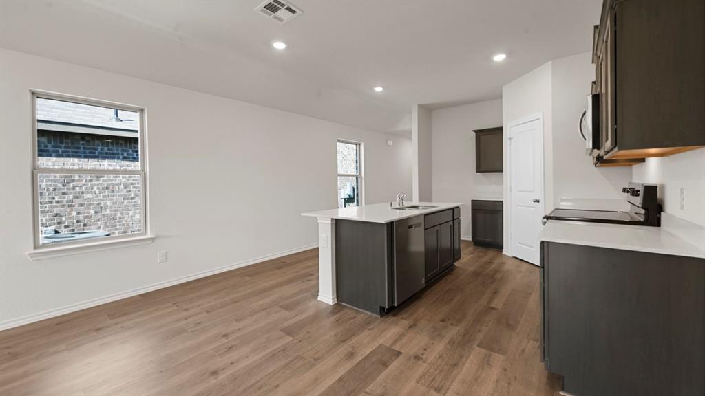 Open-concept kitchen and living area featuring wood-finish flooring, recessed lighting, a kitchen island with sink, and dark gray cabinetry