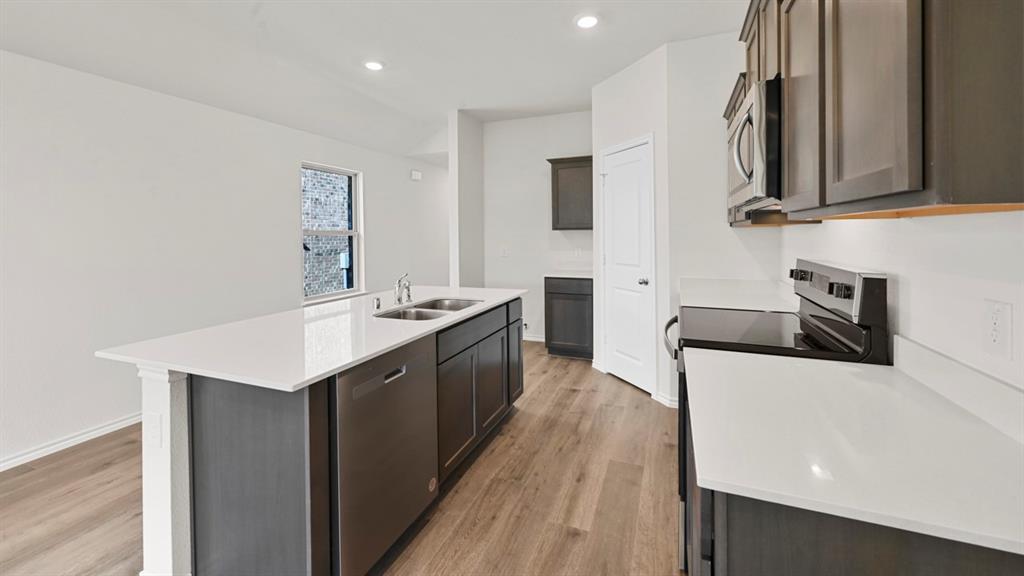 Kitchen with a central island, stainless steel sink, wood-finish flooring, and recessed lighting Kitchen with a central island, stainless steel sink, wood-finish flooring, and recessed lighting