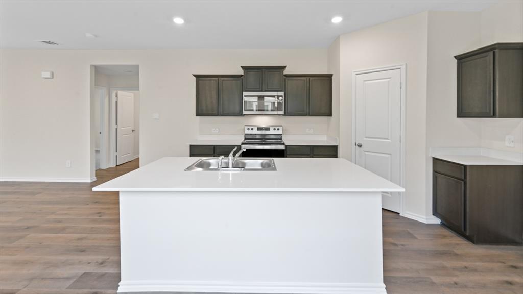 Modern kitchen island with an undermount sink, white countertops, dark wood-finish cabinetry, stainless steel appliances, and wood-finish flooring