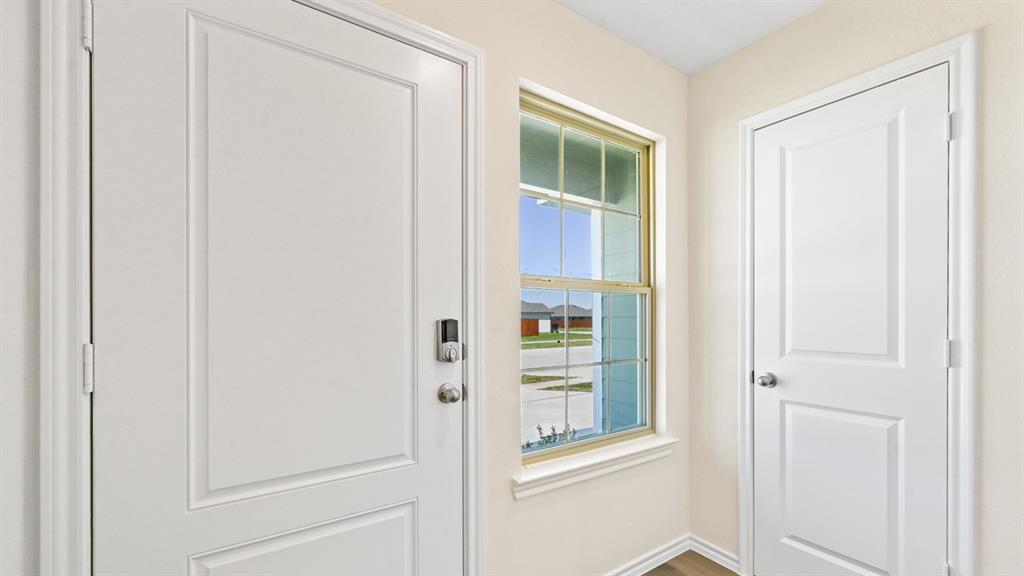 Entryway featuring a white paneled door with smart lock hardware, a double-hung window with a golden-hued frame, and light-toned walls