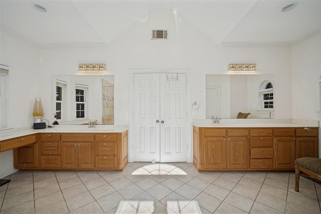 Dual vanities with wood cabinetry and light-toned solid surface countertops, vaulted ceiling, large wall-mounted mirrors, and diagonal-set tile flooring