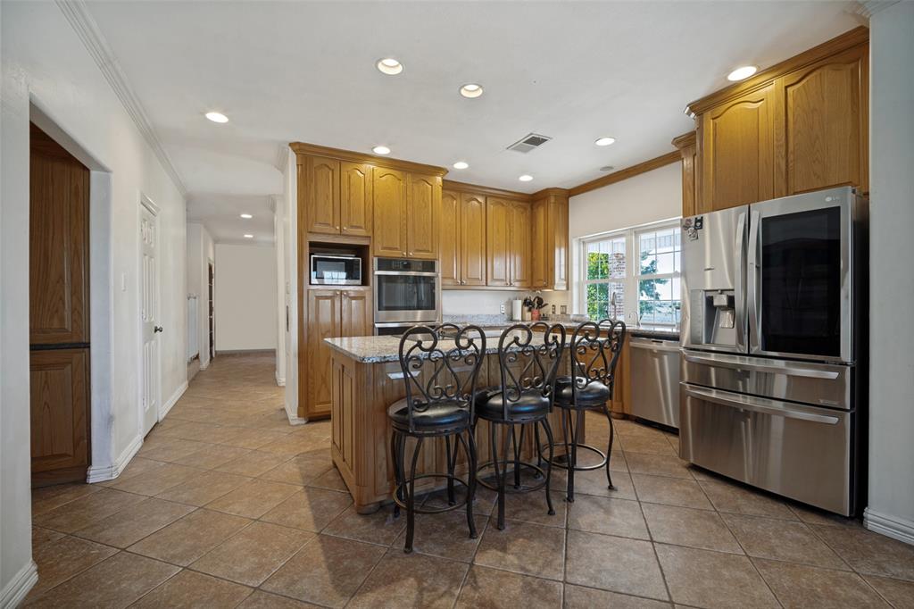 Kitchen featuring wood cabinetry, stone-surface countertops, a center island with bar seating, stainless steel appliances, and tile flooring